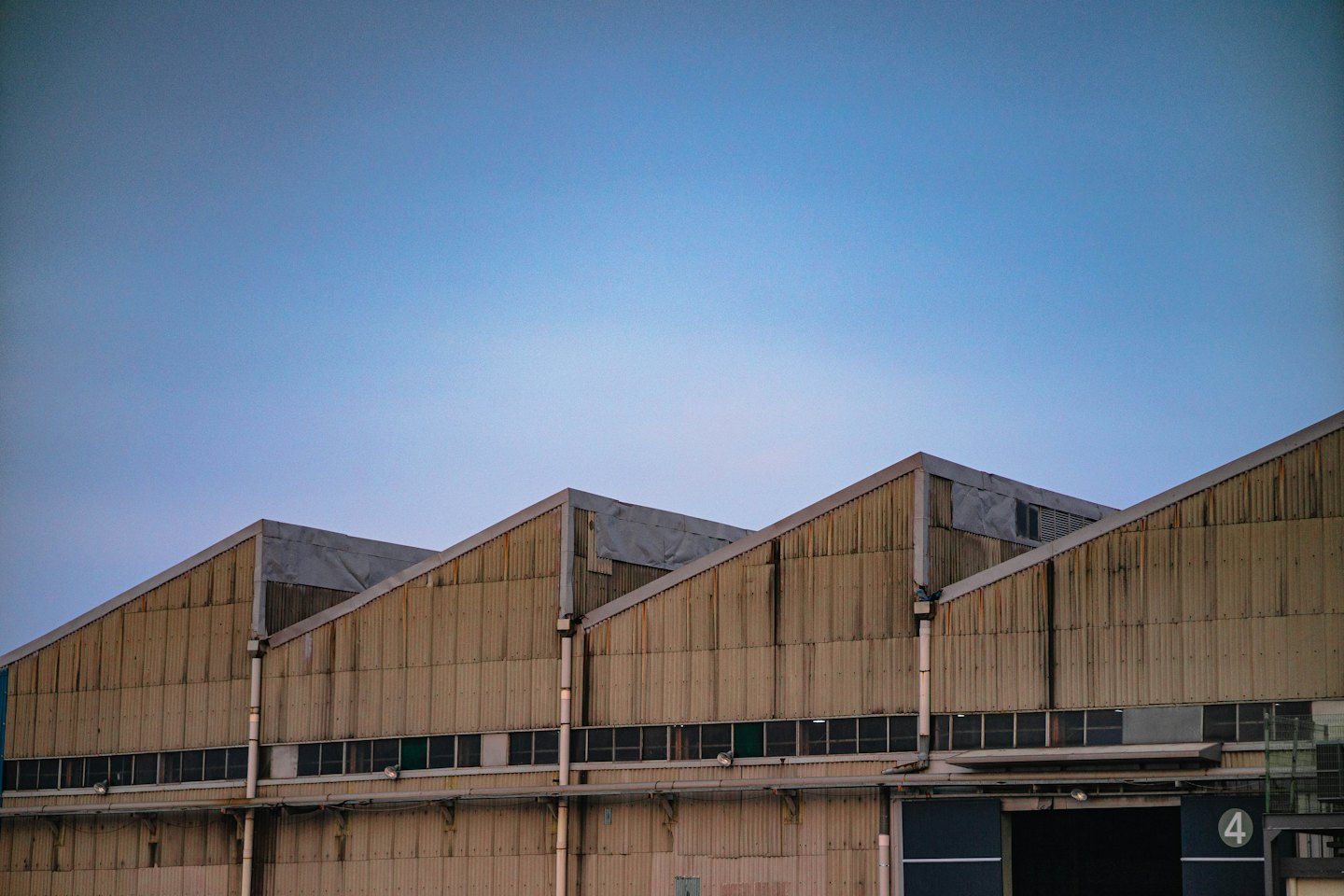 Edificios industriales con tejados a dos aguas bajo un cielo azul pálido.