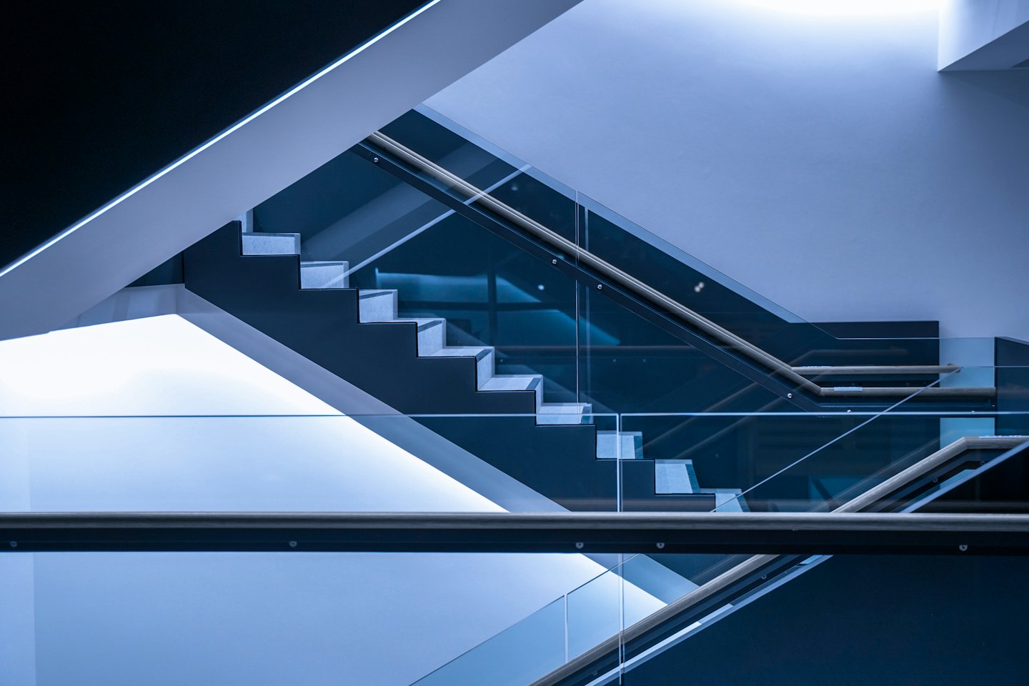 Escalera moderna con peldaños de metal oscuro y barandillas de cristal.