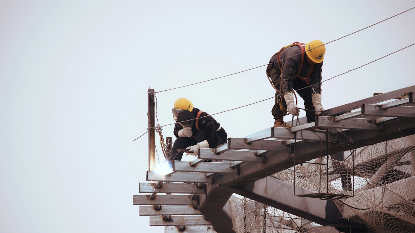 Dos obreros de la construcción soldando y trabajando en una estructura metálica.